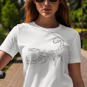 May include: A white t-shirt with a black line drawing of a scorpion on the front.