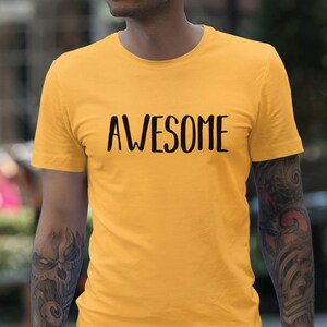 以下が含まれることがあります： 前面に黒い文字で「AWESOME」とプリントされた黄色のTシャツです。