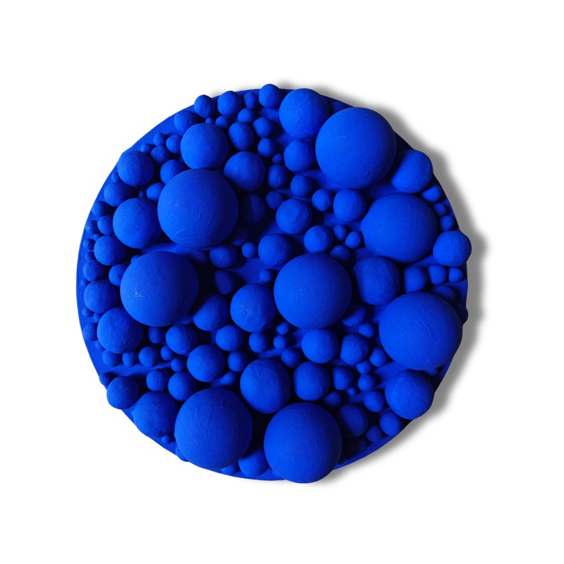 May include: A round, cobalt blue wall art piece featuring a textured surface with varying sizes of spherical shapes. The spheres are densely packed, creating a three-dimensional effect. The artwork is set against a white background.