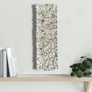 May include: A silver wall sculpture with a textured, organic design. The sculpture is rectangular and has a rough, uneven surface.