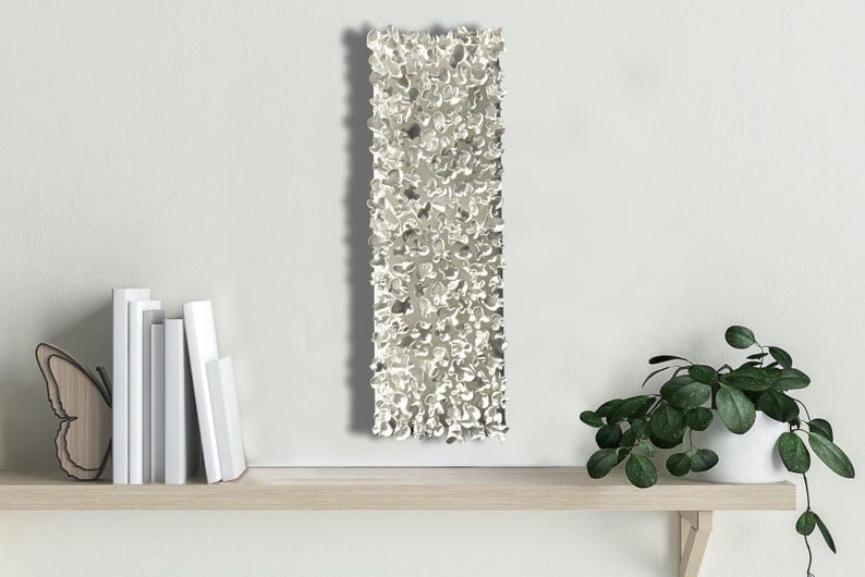 May include: A silver wall sculpture with a textured, organic design. The sculpture is rectangular and has a rough, uneven surface.