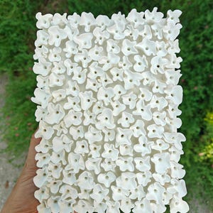 A rectangular, white clay wall art piece. The surface is densely covered with small, three-dimensional, flower-like shapes. Floral wall art | White clay wall sculpture | 3D artwork | Abstract in white | Small wall sculpture