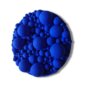 May include: A round, abstract wall art piece featuring a textured surface of varying sized blue spheres. The spheres are densely packed, creating a three-dimensional effect. The artwork is set against a white background.