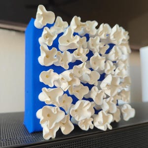 May include: A white ceramic sculpture with a blue background. The sculpture is made up of many small, organic shapes that resemble flowers.