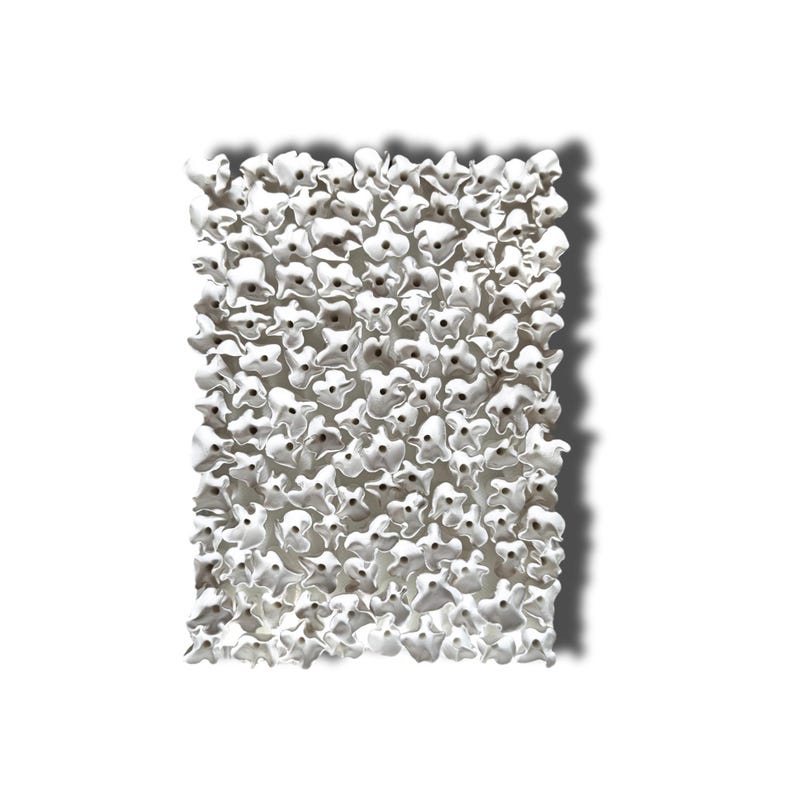 May include: A rectangular wall art piece composed of numerous white, flower-like ceramic elements. Each flower has a dark center, creating a textured, three-dimensional effect. The artwork casts a shadow on a white background.