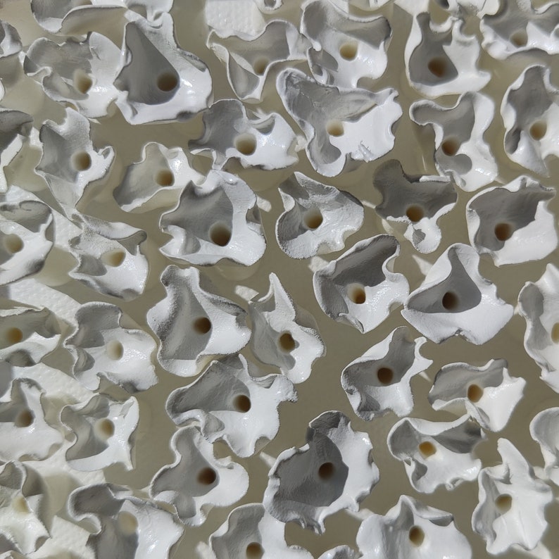 May include: An overhead shot of numerous white, petal-shaped objects with a central hole. The objects have a glossy finish with gray shading, creating a textured appearance. The background is a light, neutral color.