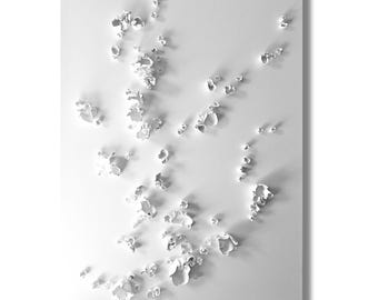 May include: A white, abstract artwork featuring raised, organic shapes scattered across a rectangular surface. The shapes cast subtle shadows, creating depth and texture. The overall effect is minimalist and modern, with a focus on form and light.