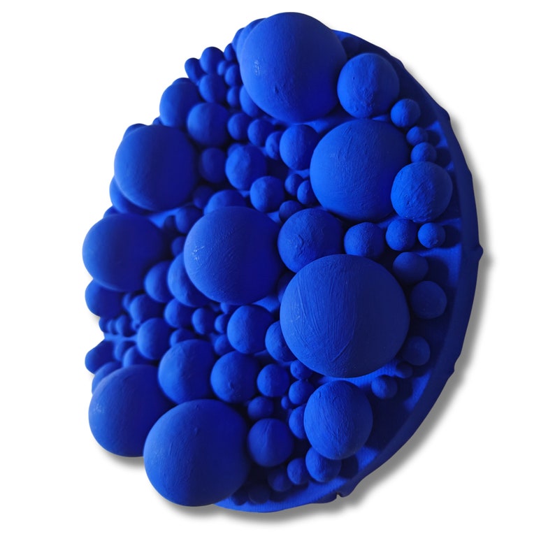 May include: A vibrant, abstract wall art piece featuring a cluster of varying-sized spheres in a deep blue hue. The spheres are densely packed, creating a textured, three-dimensional effect. The artwork is mounted on a circular base.