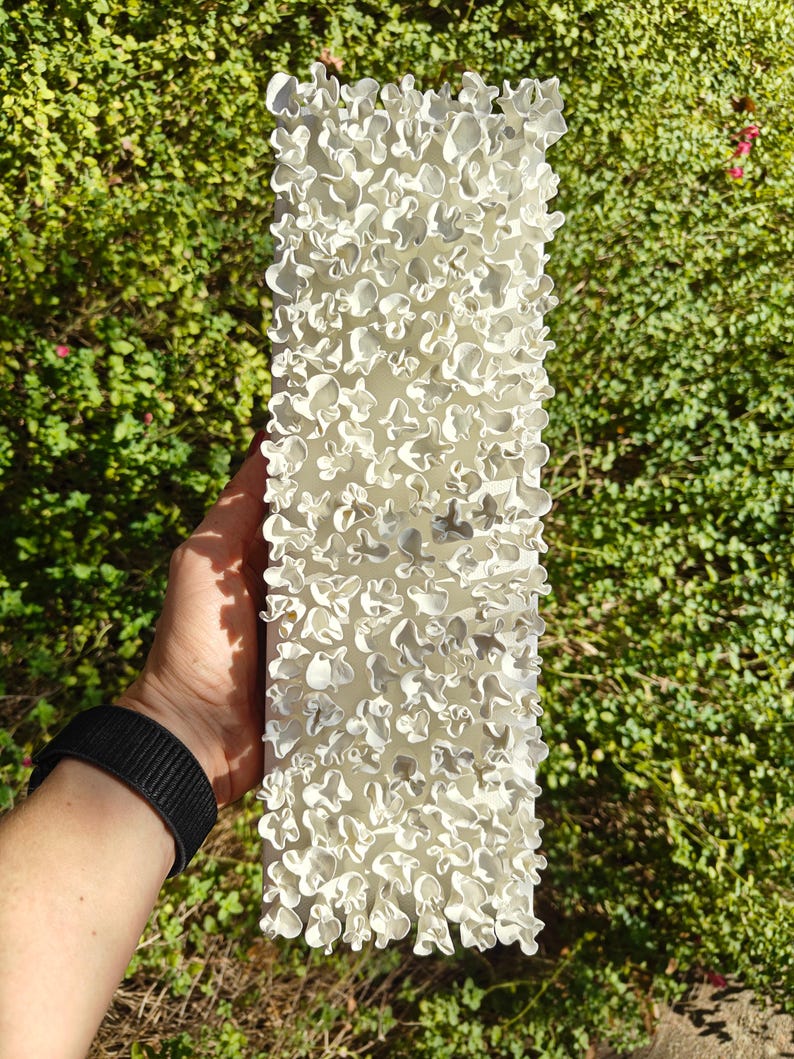 May include: White ceramic wall sculpture with a textured surface. The sculpture is made up of many small, irregular shapes that resemble flowers.