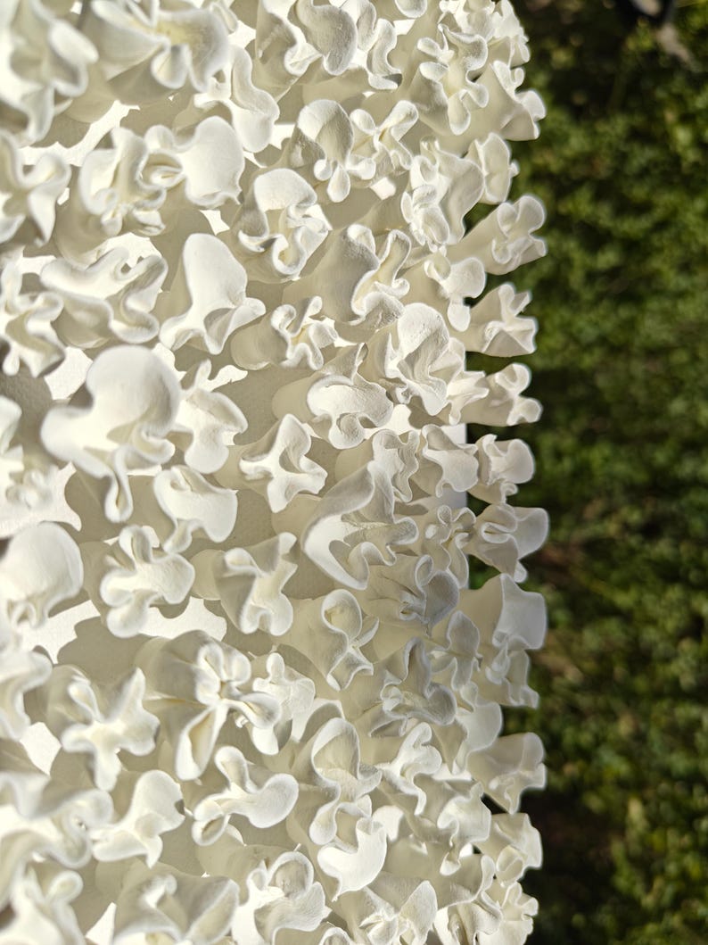 May include: A close-up of a white, 3D printed sculpture with a textured, organic design. The sculpture is made up of many small, overlapping shapes that resemble flowers or coral.
