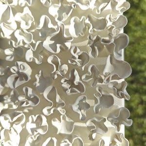 May include: A close-up of a white, textured, three-dimensional wall art piece. The piece is made of many small, overlapping, organic shapes that create a flowing, abstract design.