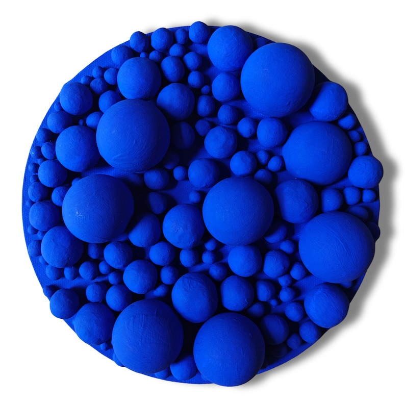 May include: A round, textured wall art piece featuring a vibrant blue color. The artwork is covered with various sized, raised spheres, creating a 3D effect. The spheres are densely packed, giving the piece a unique, tactile quality.