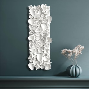 May include: A white, rectangular wall art piece with a 3D floral design. The artwork is mounted on a teal wall, with a teal vase holding dried flowers on a shelf below. The piece has a modern, abstract aesthetic.
