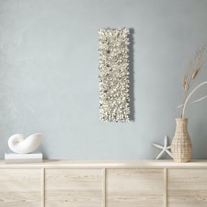 May include: A white wall sculpture with a textured, organic design. The sculpture is mounted on a light blue wall and is displayed above a wooden dresser.
