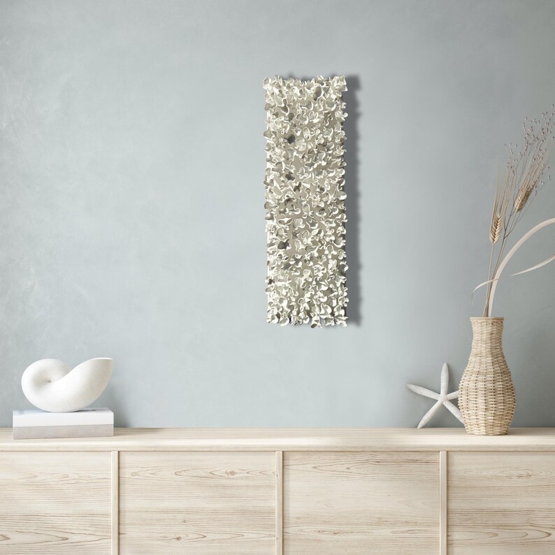May include: A white wall sculpture with a textured, organic design. The sculpture is mounted on a light blue wall and is displayed above a wooden dresser.