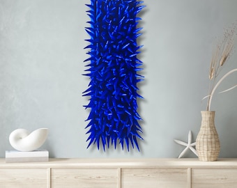 Könnte beinhalten: Ein vertikales Wandkunstwerk in leuchtendem Blau mit einem stacheligen, strukturierten Design. Das Kunstwerk ist an einer hellgrauen Wand befestigt, was einen auffälligen Kontrast erzeugt. Dieses Stück verleiht jedem Innenraum eine moderne Note.
