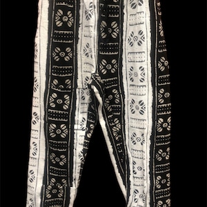 Może przedstawiać: Czarno-białe spodnie w paski z geometrycznym wzorem. Spodnie mają sznurek w pasie i luźny krój.