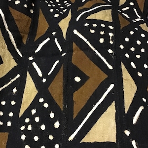 Puede incluir: Primer plano de un textil con un patrón geométrico. El diseño presenta formas negras, beige y blancas, incluyendo triángulos, diamantes y líneas punteadas. La tela tiene una apariencia texturizada, sugiriendo un material tejido.