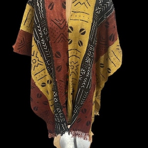 May include: A vibrant poncho with a V-neck. It has a patchwork design in brown, yellow, and black, with geometric and abstract patterns. The bottom edge is finished with a fringe, adding texture to the garment.