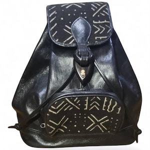 May include: Black leather backpack with a flap closure and a small front pocket. The flap and pocket feature a black and white geometric pattern. The backpack has a leather strap and a wooden toggle closure.