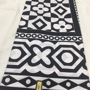 Puede incluir: Tela geométrica en blanco y negro con un patrón repetitivo de círculos, cuadrados y flores. La tela tiene un borde con un patrón repetitivo de círculos y diamantes. La tela está etiquetada como "AFRICA"
