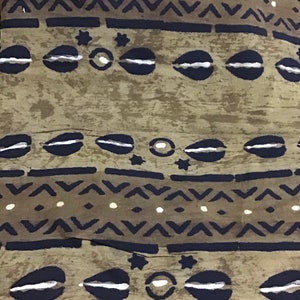 Könnte beinhalten: Ein brauner Stoff mit einem sich wiederholenden Muster aus schwarzen und weißen geometrischen Formen und stilisierten Augenmotiven.