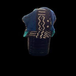 May include: A blue and white patterned hat with a brim. The hat features a geometric design in white on a dark blue background. The brim is a solid teal color. The hat is set against a black background.