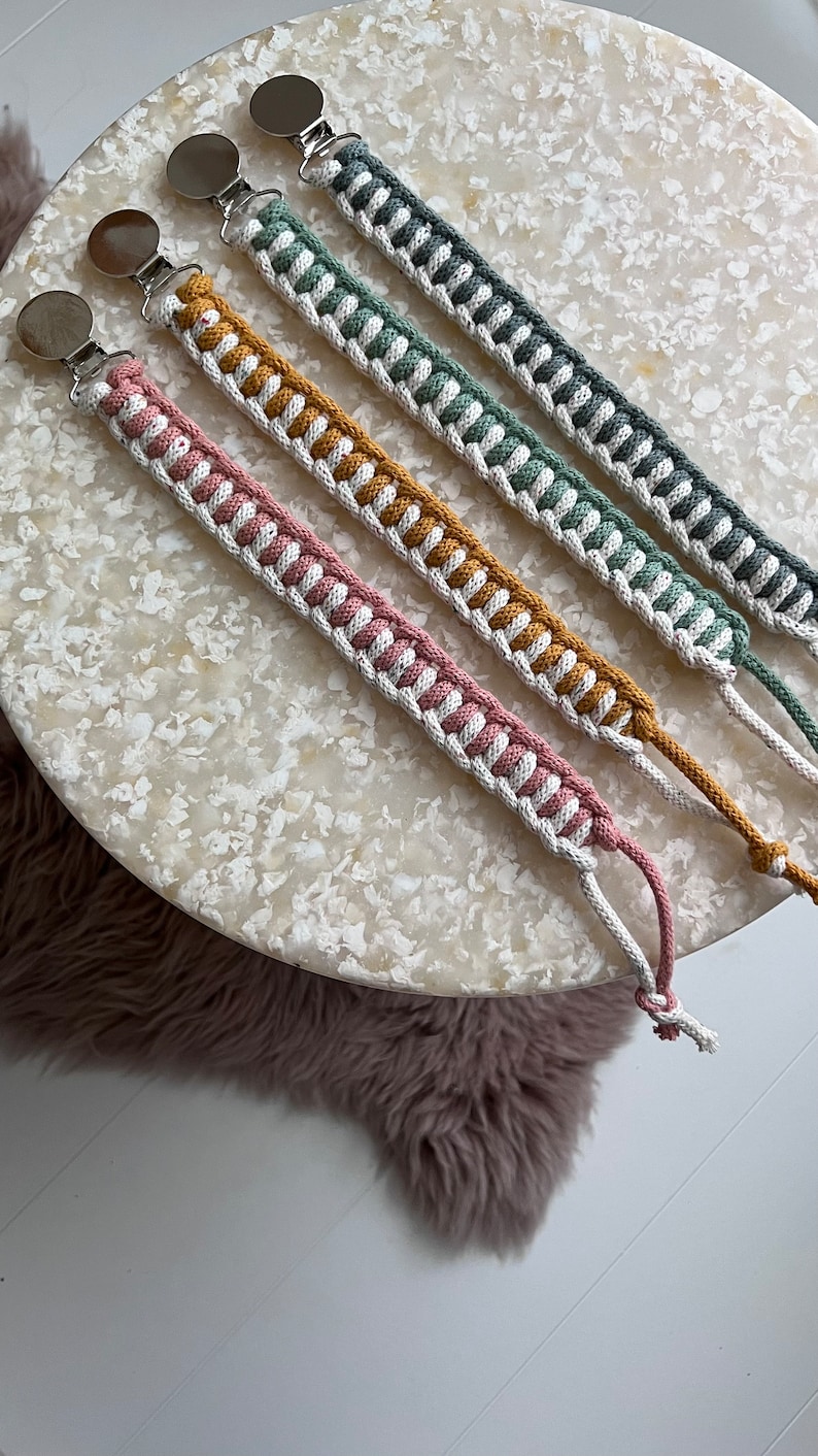 May include: Four crocheted dummy clips with silver clips. The clips are in shades of pink, yellow, green, and grey.
