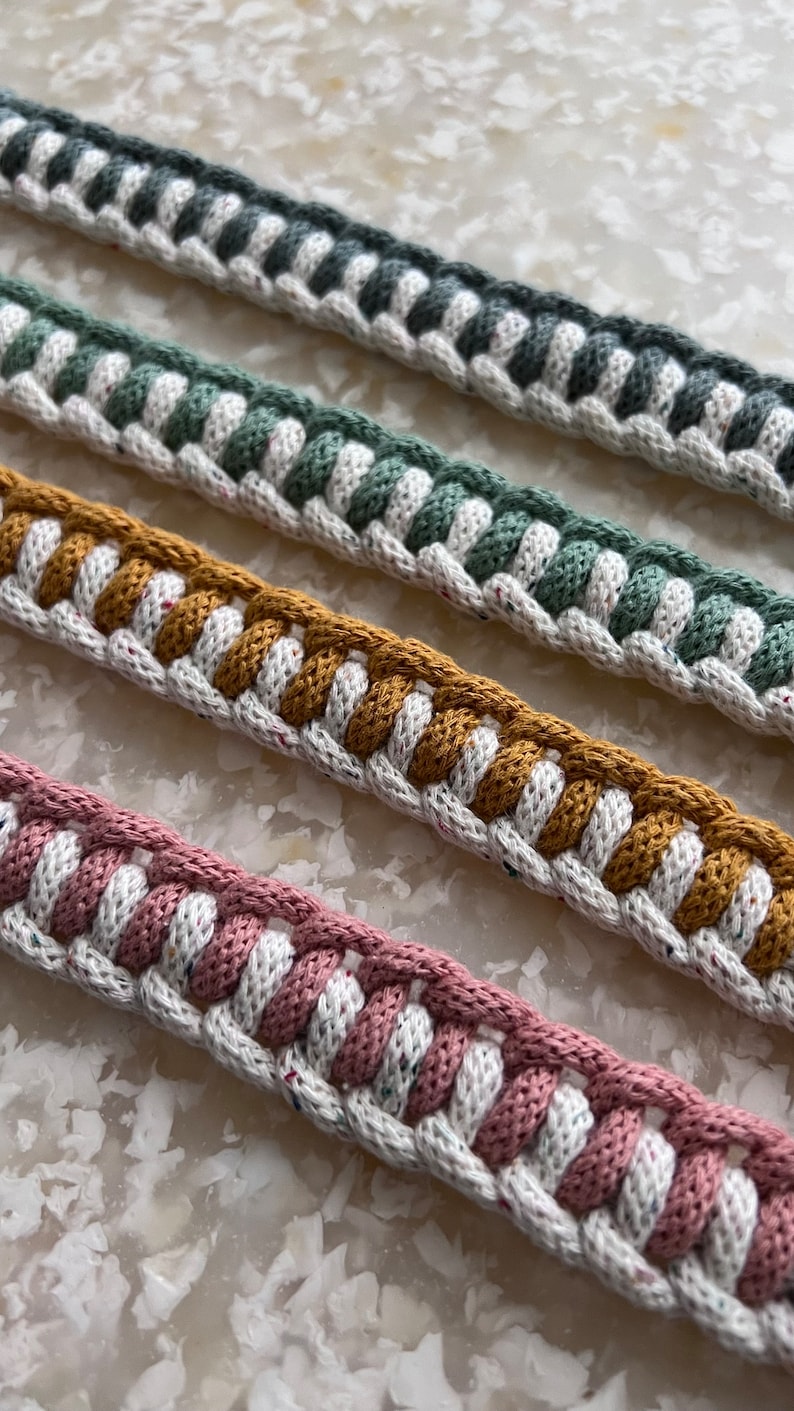 May include: Four different colours of braided rope trim with white speckles. The colours are grey, green, mustard yellow, and pink.
