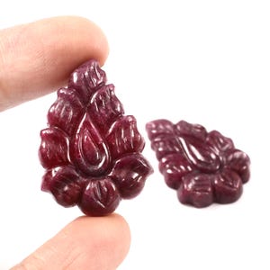 May include: Two carved ruby gemstone pendants shaped like a flower. The pendants are a deep red colour and have intricate details.