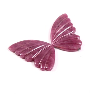 May include: A pair of carved, ruby-coloured butterfly wings. The wings are made of a polished, translucent material with detailed veining. The wings are arranged to resemble a butterfly, with a white background.