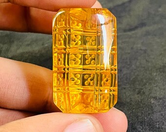 May include: A large, yellow, faceted gemstone with a geometric pattern. The gemstone is cut in a rectangular shape and has a smooth, polished surface.