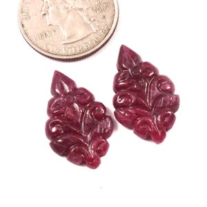 Peut inclure: Deux pendentifs en pierres précieuses rubis sculptées en forme de feuille florale. Les pendentifs sont d'un rouge profond et sont à côté d'une pièce de monnaie de 25 cents pour la comparaison des tailles. Les pierres précieuses ont des sculptures détaillées.