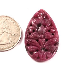 以下が含まれることがあります： 花柄の彫刻が施された、涙滴型のピンク色の宝石のペンダント。ペンダントは、アメリカの25セント硬貨と同じくらいの大きさです。