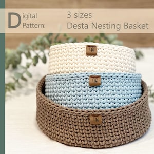 May include: Three crocheted nesting baskets in brown, blue, and white. The baskets are stacked on top of each other. The text "Digital Pattern: DESTA NESTING BASKET" is visible at the top of the image.