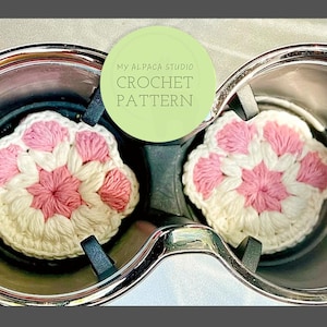 May include: Two crocheted pink and white flower-shaped cup coasters in a car cup holder. The text "My Alpaca Studio Crochet Pattern" is on a green circle.
