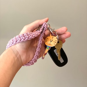 May include: A pink crocheted key chain with a cat-shaped key charm and a silver key ring. The keychain is attached to a black key fob.