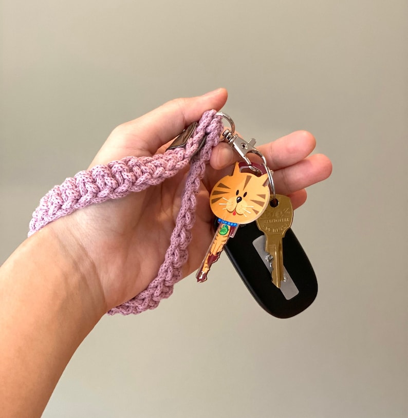 May include: A pink crocheted key chain with a cat-shaped key charm and a silver key ring. The keychain is attached to a black key fob.