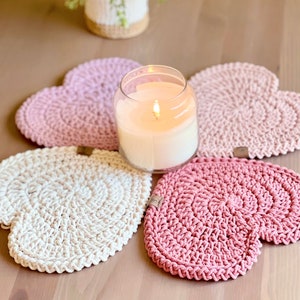 May include: Four crocheted heart-shaped coasters in pink and white with a lit candle in a glass jar in the center.