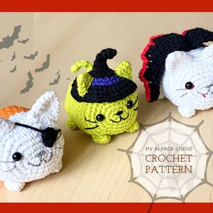 Puede incluir: Tres juguetes de gato de crochet disfrazados para Halloween. Uno es una bruja con un sombrero negro, otro es un vampiro con una capa roja y otro es un pirata con un parche en el ojo. Los juguetes están sentados sobre una superficie de madera con un diseño de telaraña.