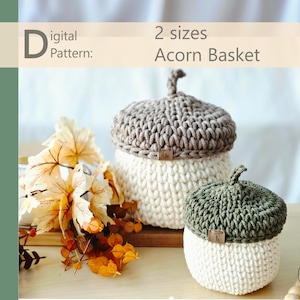 以下が含まれることがあります： 茶色と緑色の帽子とオフホワイトのボディが付いた、大小2つのかぎ針編みのどんぐりバスケット。画像には「Digital Pattern: 2 sizes Acorn Basket」というテキストが含まれています。背景には装飾的な秋の葉があります。