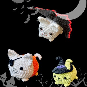 Puede incluir: Tres juguetes de crochet con forma de gato disfrazados para Halloween. Un gato blanco con una capa negra y ribete rojo, un gato blanco con un disfraz de caramelo de ma&iacute;z naranja y blanco, y un gato verde con un sombrero de bruja negro.