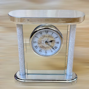 May include: A silver mirrored clock with a white face and Roman numeral markings. The clock is on a silver stand with a mirrored surface. The clock face says "Danbury Quartz".