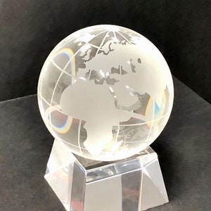 May include: A clear glass globe with a frosted white etched world map on a clear glass base. The globe is on a black surface.