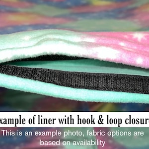 Puede incluir: Un forro de tela suave con un estampado de galaxia en tonos pastel rosa, azul y morado con estrellas blancas. El forro incluye una tira de cierre de velcro negra a lo largo del borde. El texto dice: Example of liner with hook & loop closure.