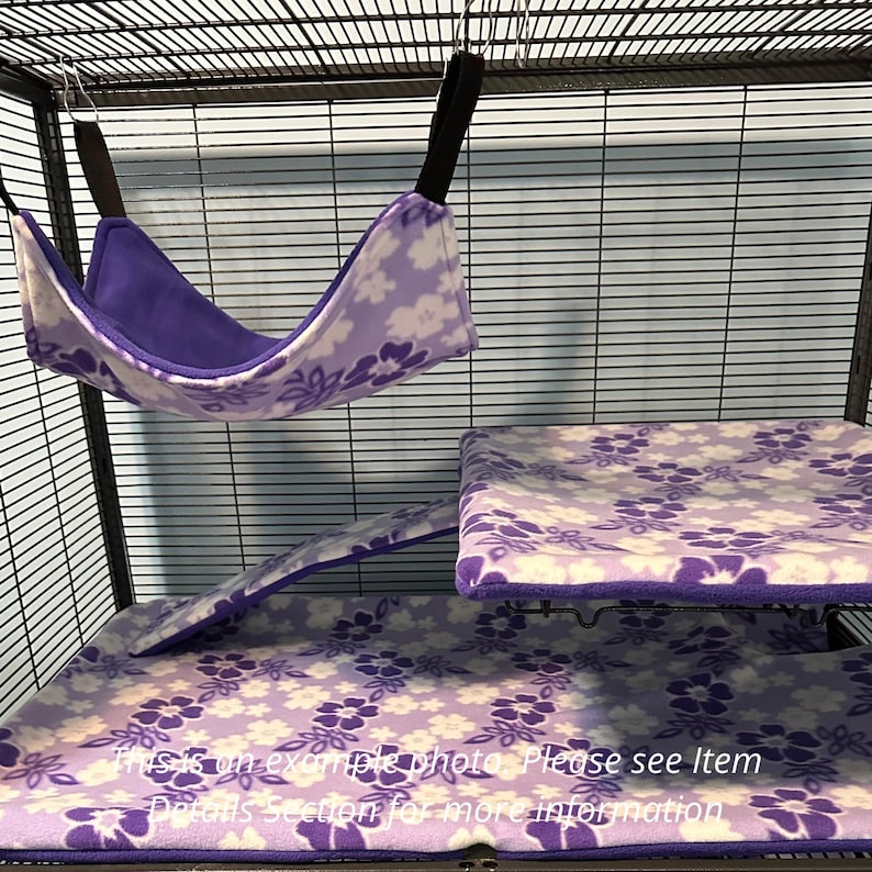 Puede incluir: Una hamaca de forro polar para mascotas con estampado floral morado y blanco, una funda de plataforma rectangular a juego y una funda de rampa dentro de una jaula de alambre. El texto en la imagen dice: This is an example photo. Please see Item Details.