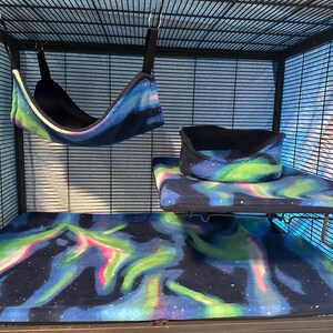 Puede incluir: Un conjunto de accesorios para jaula de animales peque&ntilde;os que incluye una hamaca colgante, una alfombrilla rectangular y una plataforma elevada con cama circular, hechos de tela suave con patr&oacute;n de aurora boreal y bordes negros.