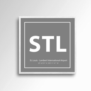 Puede incluir: Un cuadrado gris con un borde blanco y el texto "STL" en blanco, centrado en el cuadrado. Debajo del texto se encuentra "St. Louis - Lambert International Airport" y las coordenadas "38°44′50″ N 090 21'41" W".