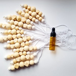 May include: A set of wooden bead necklaces with white string, each necklace has a different combination of round and square beads in cream and white colors. A small amber glass bottle with a black dropper is in the center of the image.