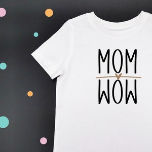 Peut inclure: T-shirt blanc avec un texte noir qui dit "MOM WOW" avec un petit cœur brun entre les mots.
